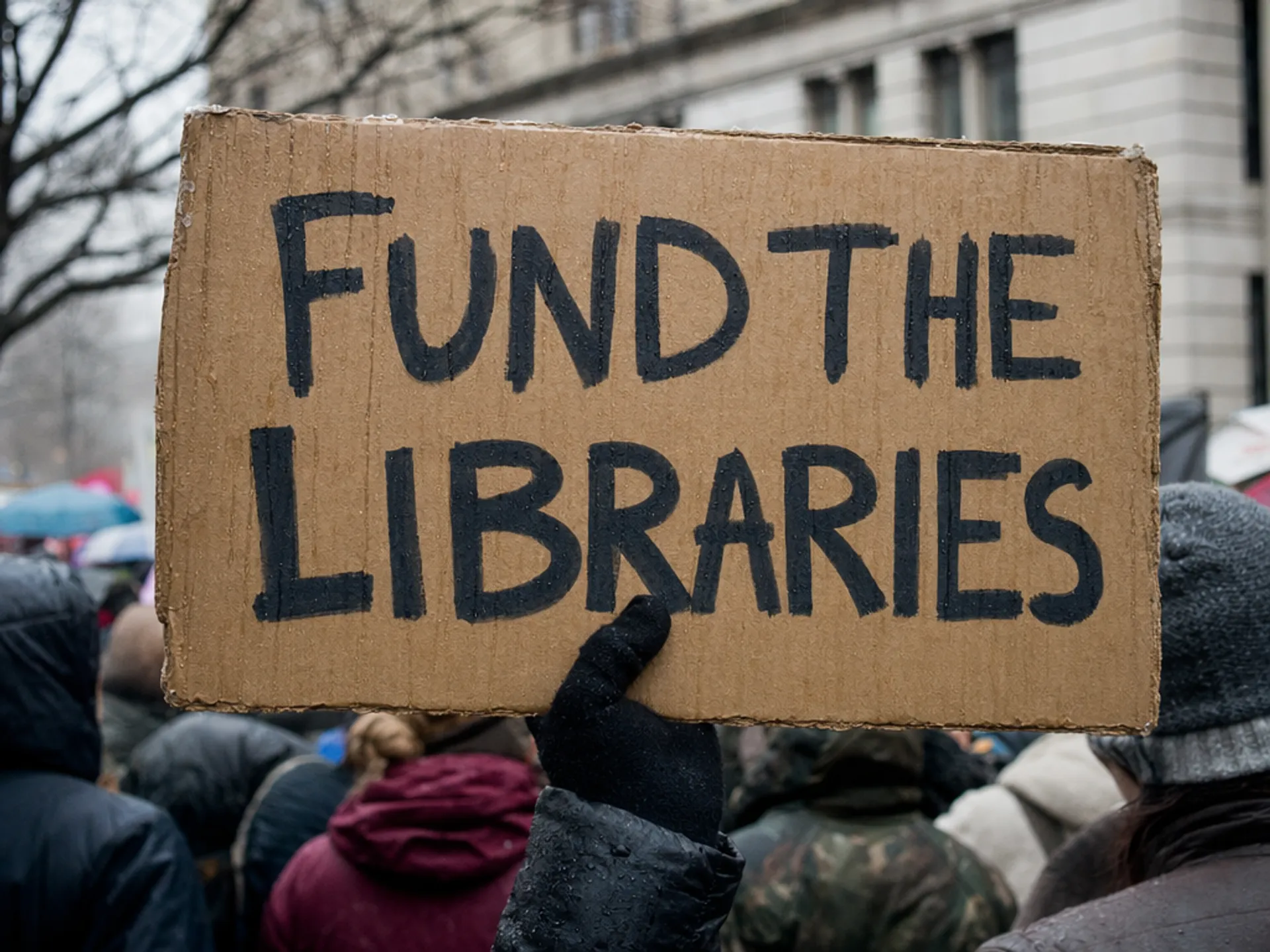 AI-generated documentary photograph of a handmade protest sign with legible text in winter rain