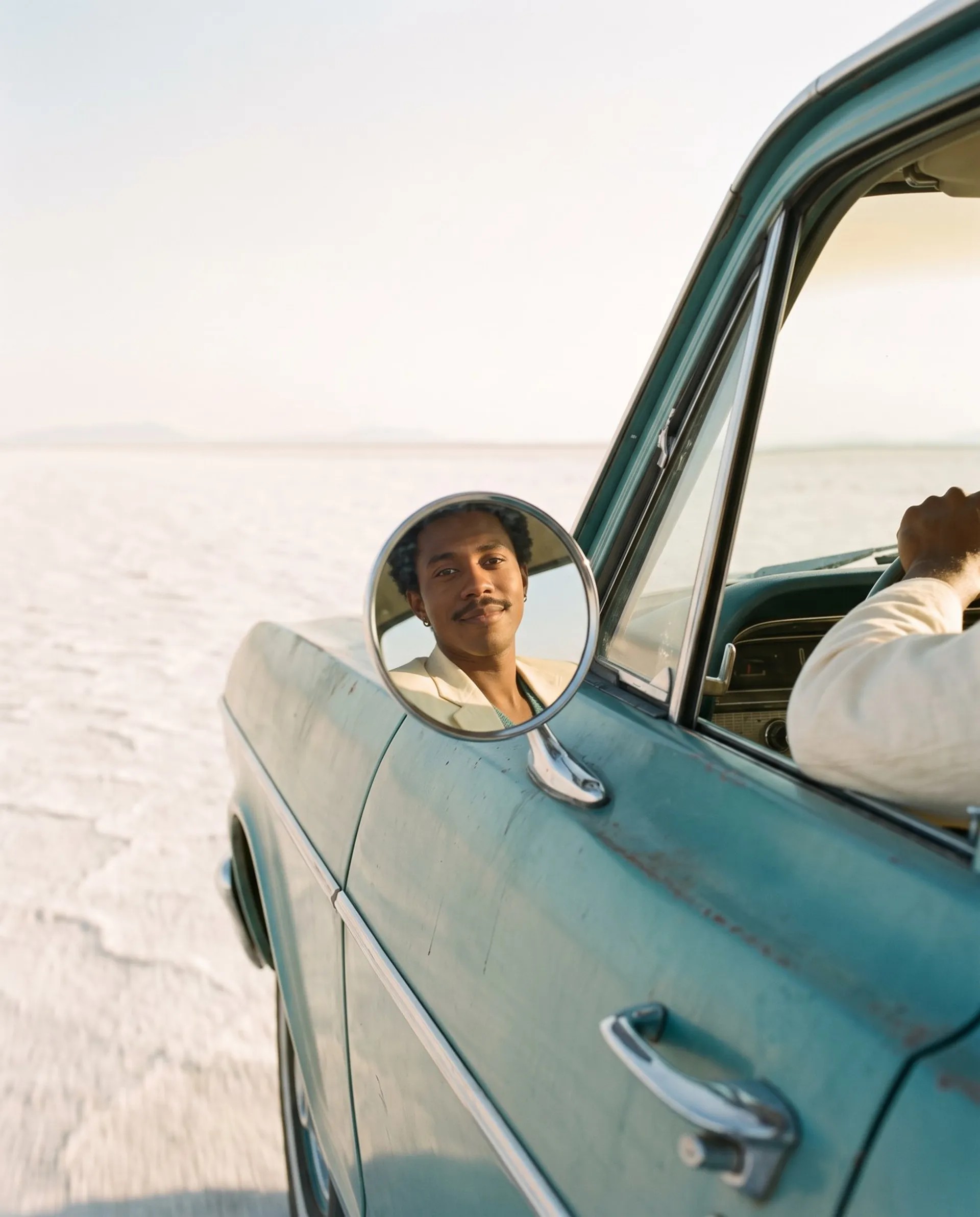 The same AI-generated man reflected in the wing mirror of a vintage teal car on a salt flat