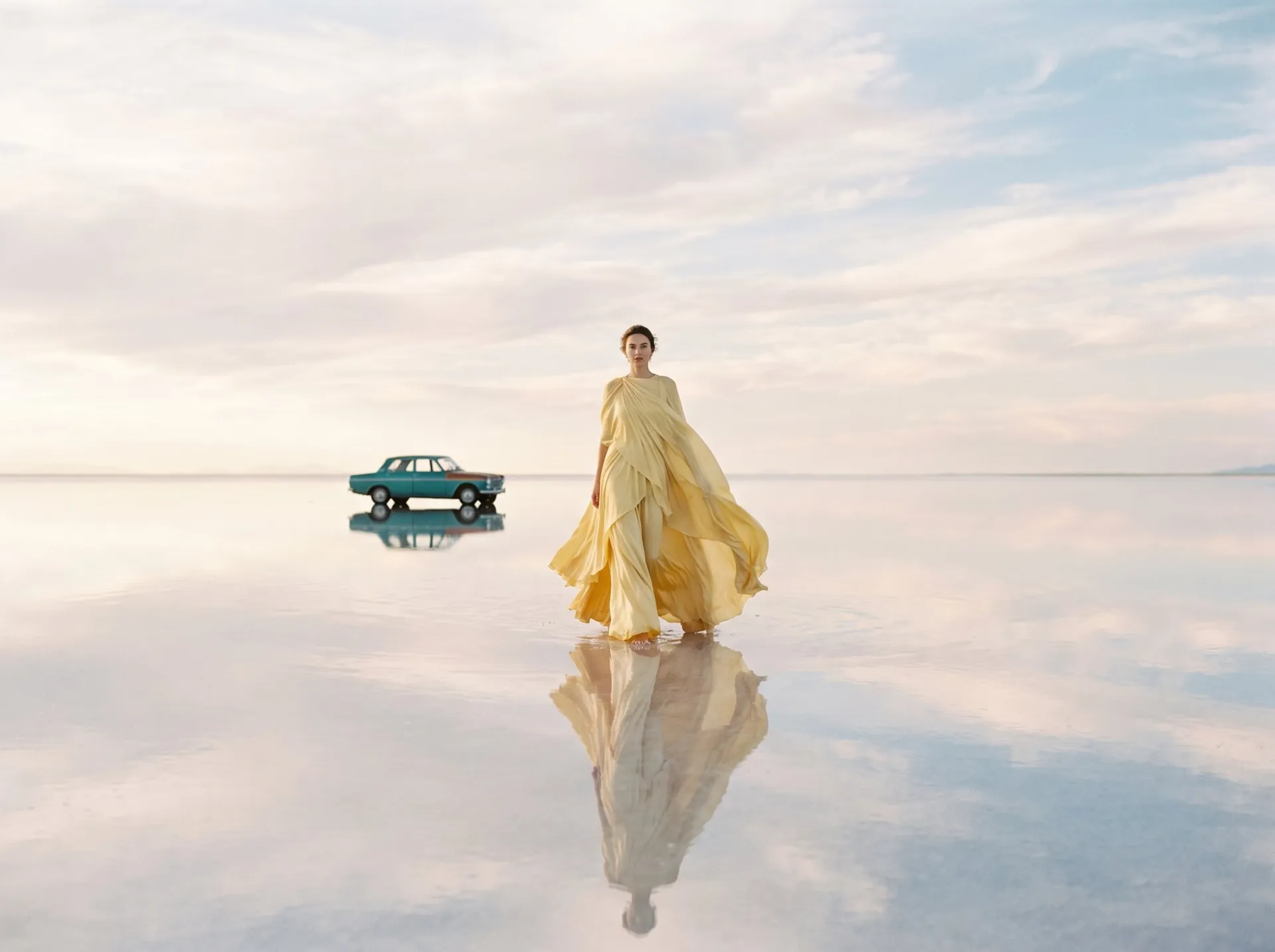 AI-generated fashion photo of a model in a flowing yellow silk gown walking across a mirrored salt flat, her reflection below