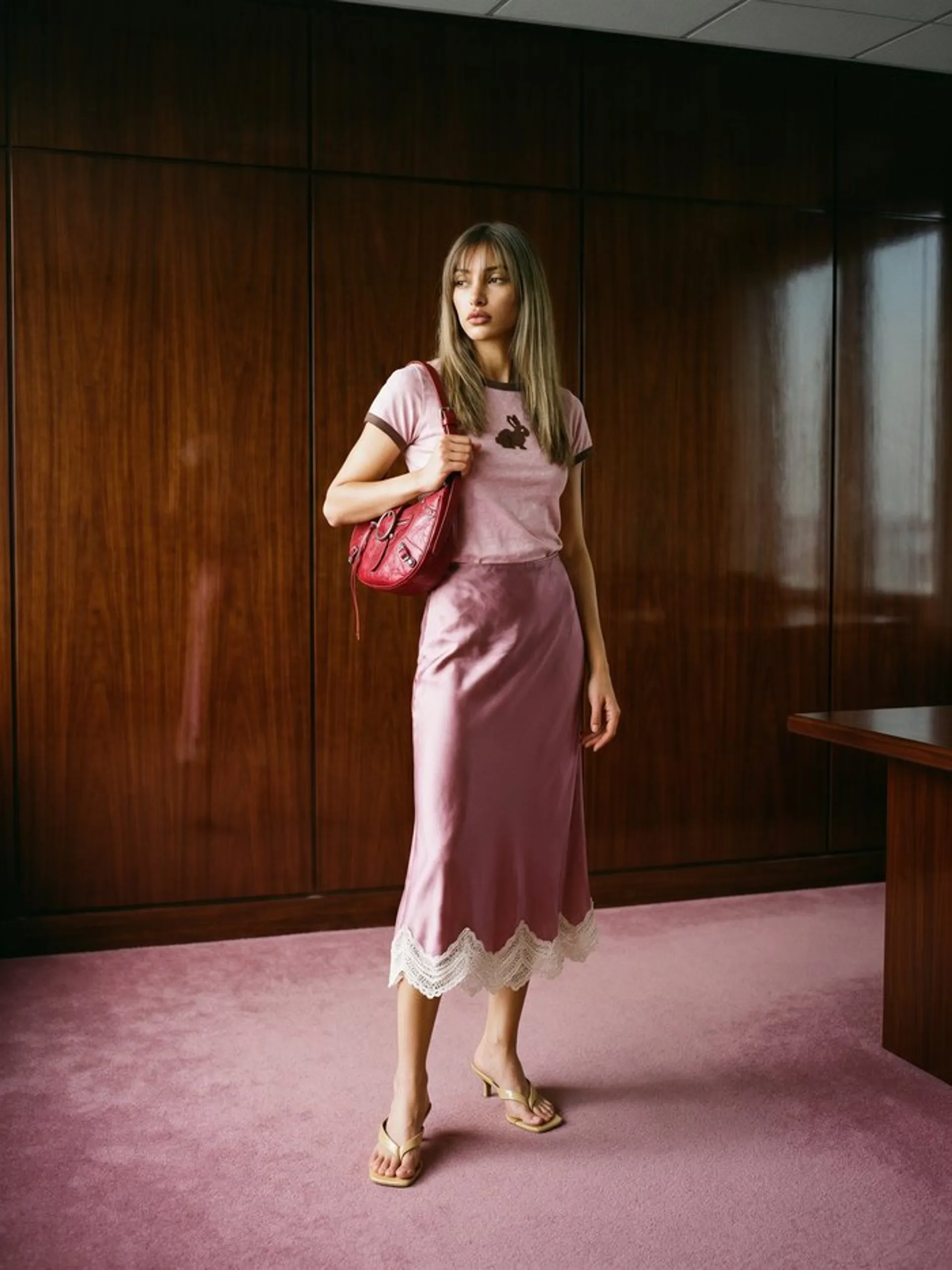 Krea 3 image of the same woman full-length in a pink ringer tee and satin slip skirt in a mahogany-panelled office